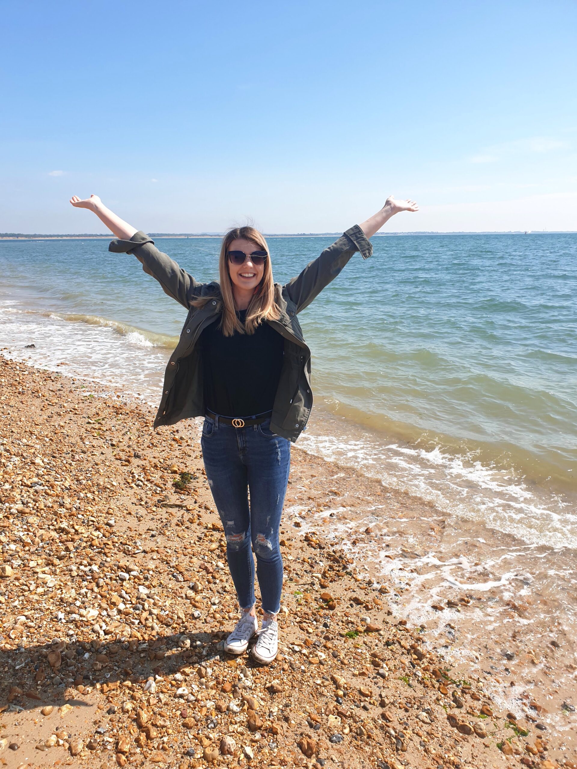 Chloe smiling with arms outsretched on a stony beach